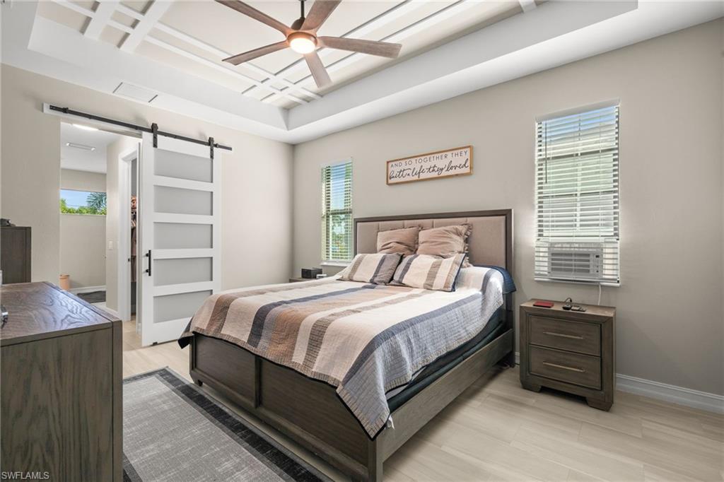 Bedroom featuring a barn door, coffered ceiling, light wood finished floors, ceiling fan, and a tray ceiling