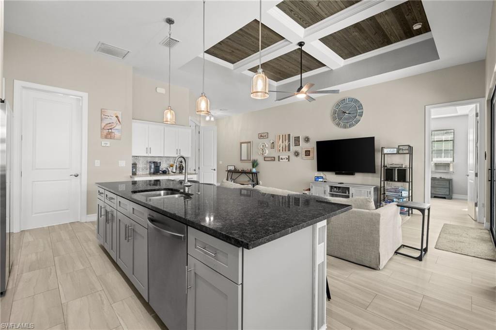 Kitchen featuring open floor plan, coffered ceiling, gray cabinetry, dark stone countertops, and pendant lighting