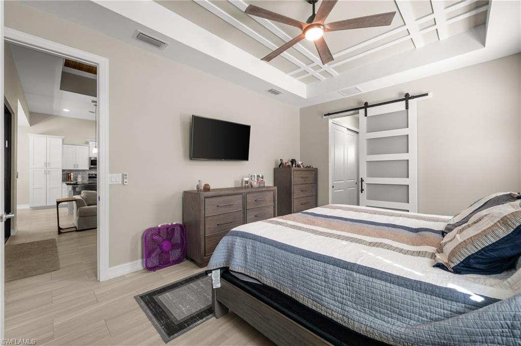 Bedroom with a barn door, coffered ceiling, ceiling fan, and light wood-type flooring