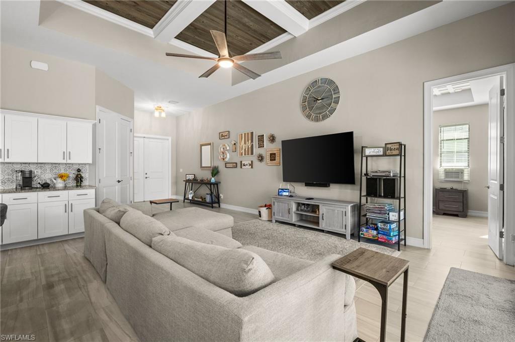 Living room with ceiling fan, a towering ceiling, a wooden ceiling with exposed beams, coffered ceiling, and light wood finished floors