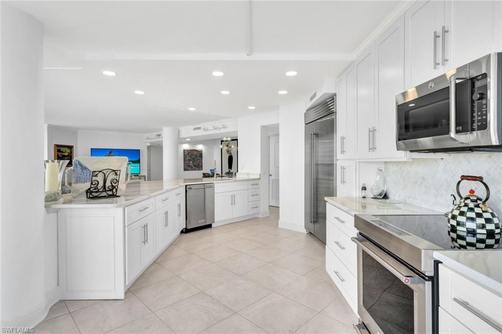 Kitchen with appliances with stainless steel finishes, light tile patterned floors, white cabinets, and backsplash