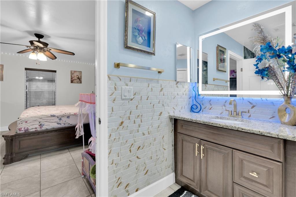Ensuite bathroom featuring vanity, tile walls, light tile patterned floors, ceiling fan, and wainscoting