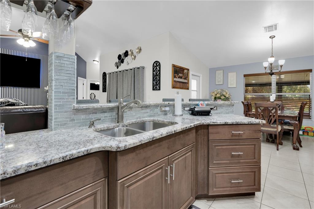 Kitchen featuring light stone countertops, light tile patterned floors, ceiling fan, lofted ceiling, and decorative light fixtures