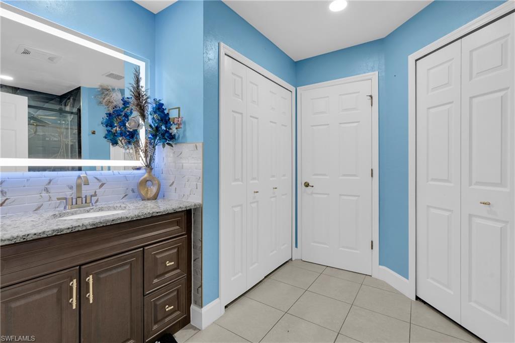 Bathroom featuring a closet, vanity, light tile patterned flooring, decorative backsplash, and recessed lighting