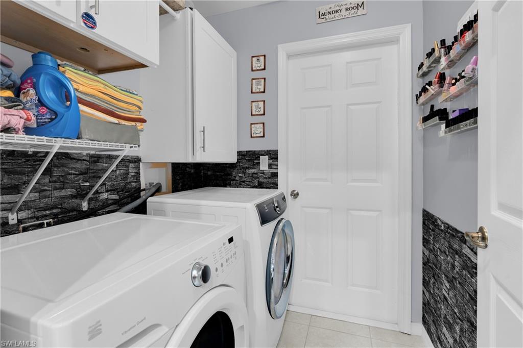 Washroom with cabinet space, light tile patterned floors, and washer and clothes dryer