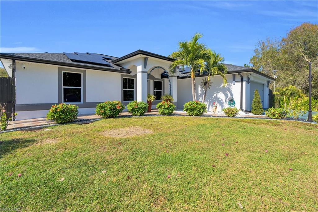 Ranch-style home with solar panels, stucco siding, and a front lawn
