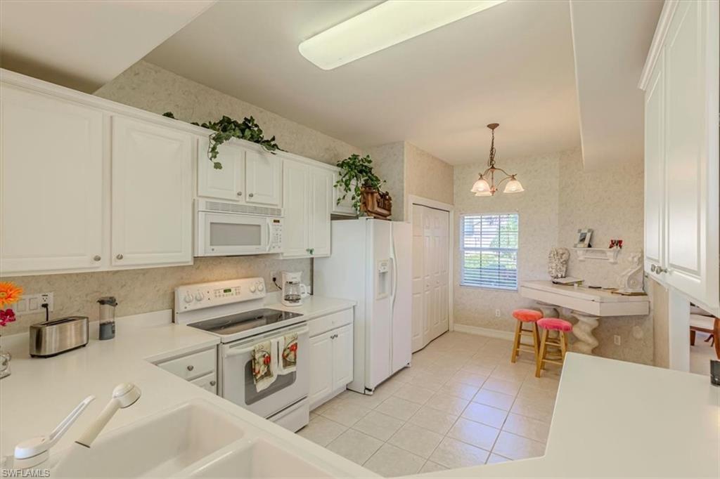 Kitchen with wallpapered walls, white appliances, light countertops, white cabinetry, and pendant lighting
