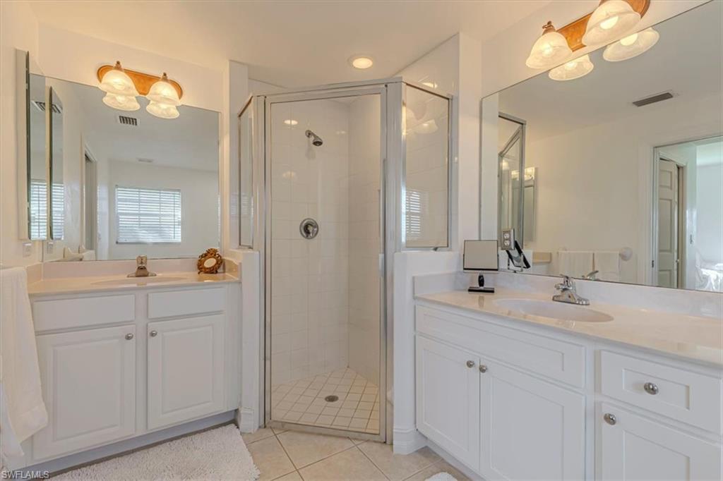 Full bath featuring two vanities, a shower stall, and light tile patterned flooring
