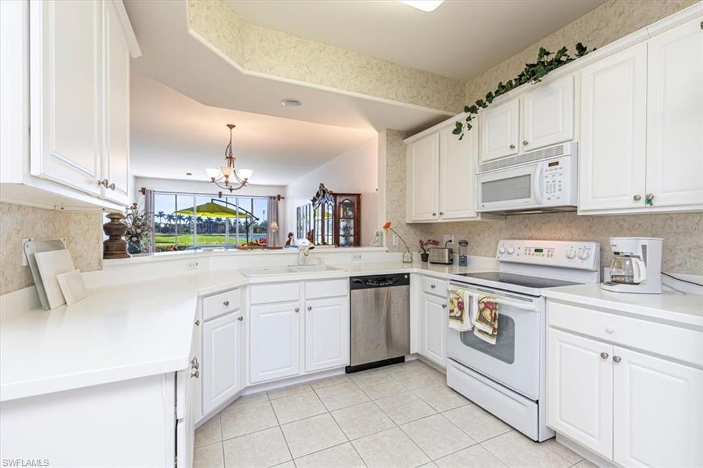 Kitchen featuring white appliances, white cabinets, light countertops, a chandelier, and wallpapered walls