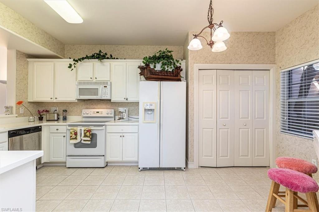 Kitchen with wallpapered walls, white appliances, decorative light fixtures, light countertops, and a chandelier