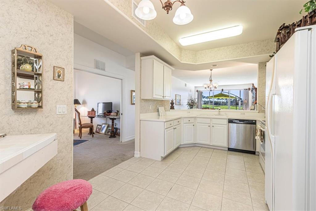 Kitchen featuring a chandelier, light carpet, stainless steel appliances, decorative light fixtures, and white cabinets