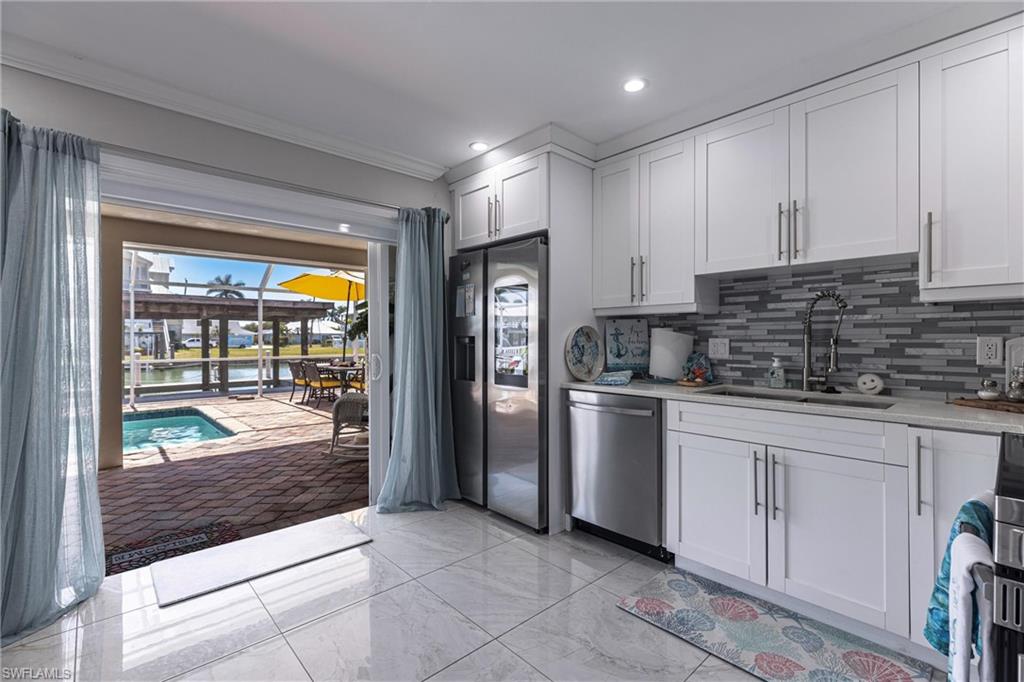 Kitchen with decorative backsplash, light countertops, ornamental molding, stainless steel appliances, and a sink