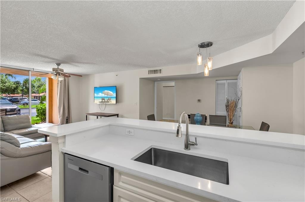 Kitchen featuring open floor plan, dishwasher, a textured ceiling, a ceiling fan, and light stone countertops