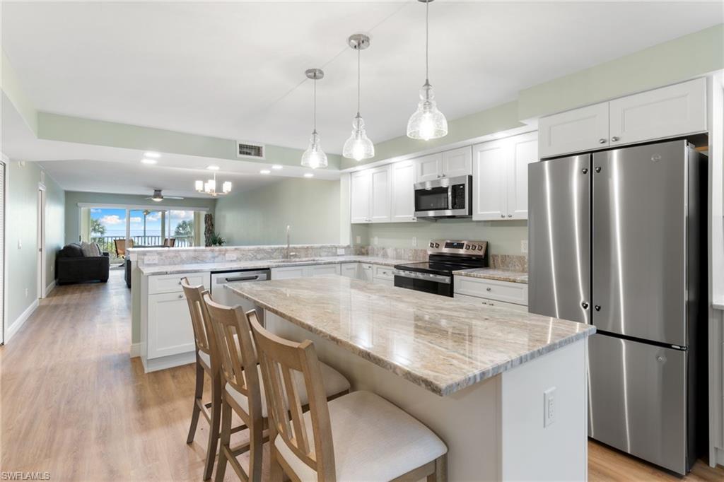 Kitchen featuring stainless steel appliances, open floor plan, a breakfast bar area, white cabinetry, and light wood-style floors