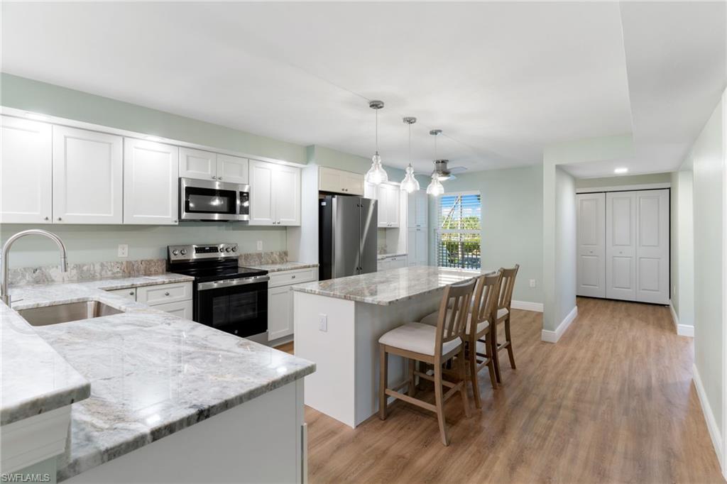 Kitchen with appliances with stainless steel finishes, pendant lighting, a kitchen bar, light stone countertops, and a center island