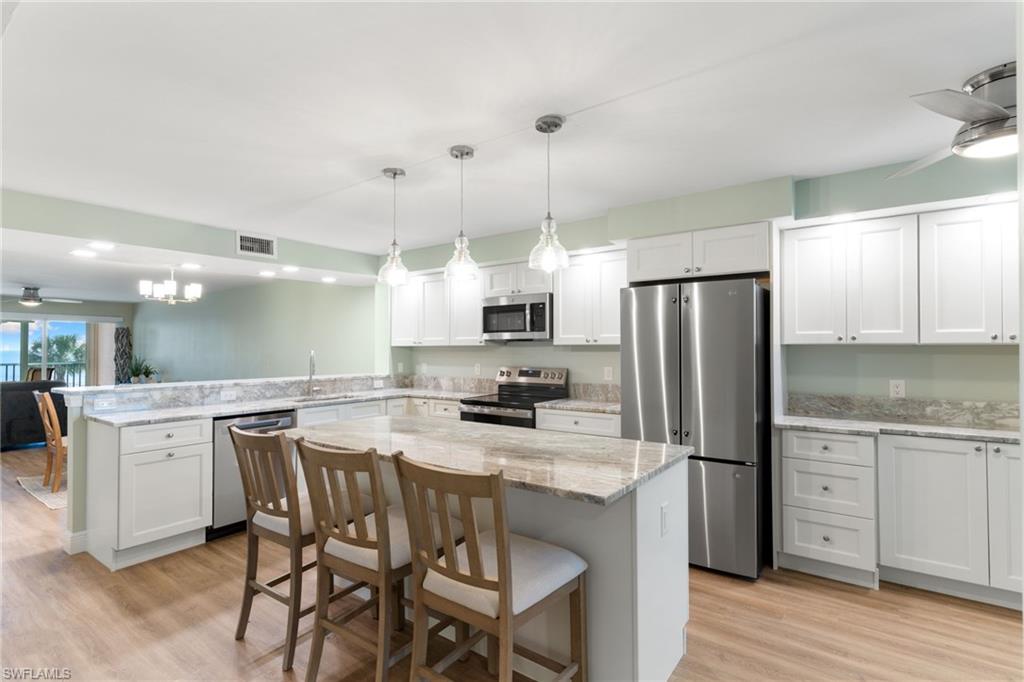 Kitchen featuring ceiling fan, a kitchen bar, stainless steel appliances, a chandelier, and light wood-type flooring