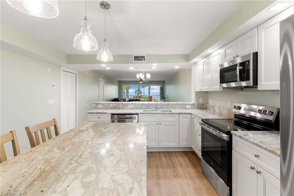 Kitchen featuring stainless steel appliances, decorative light fixtures, white cabinetry, a chandelier, and light wood-style floors
