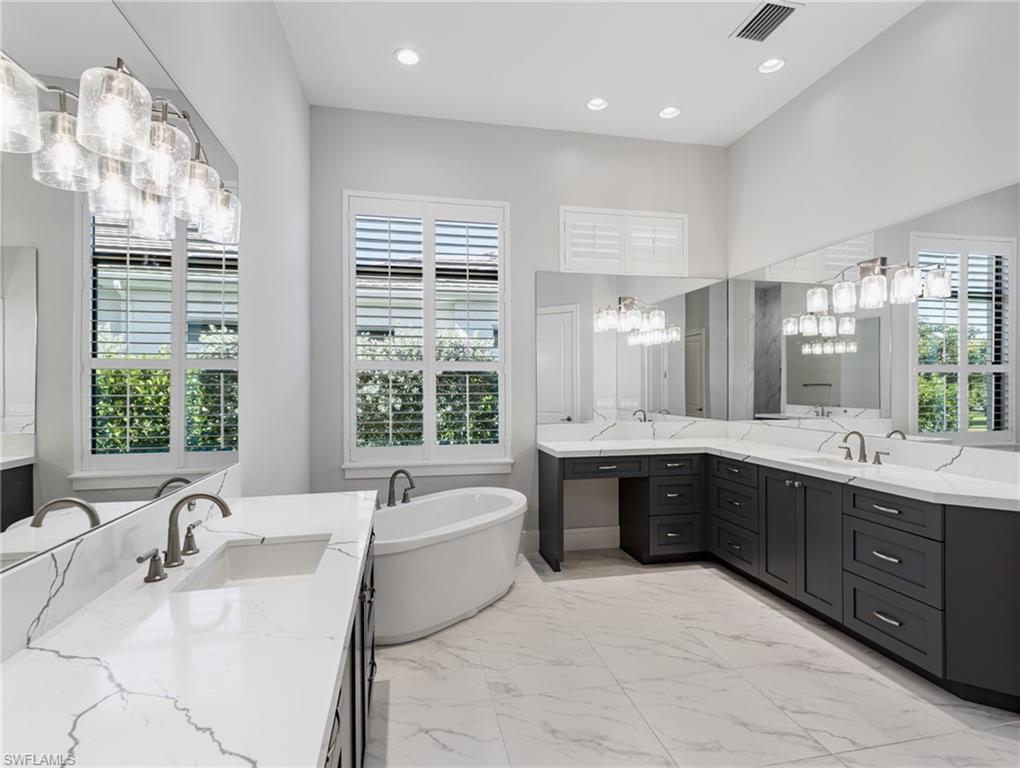 Bathroom featuring two vanities, a freestanding tub, light marble finish flooring, recessed lighting, and a chandelier