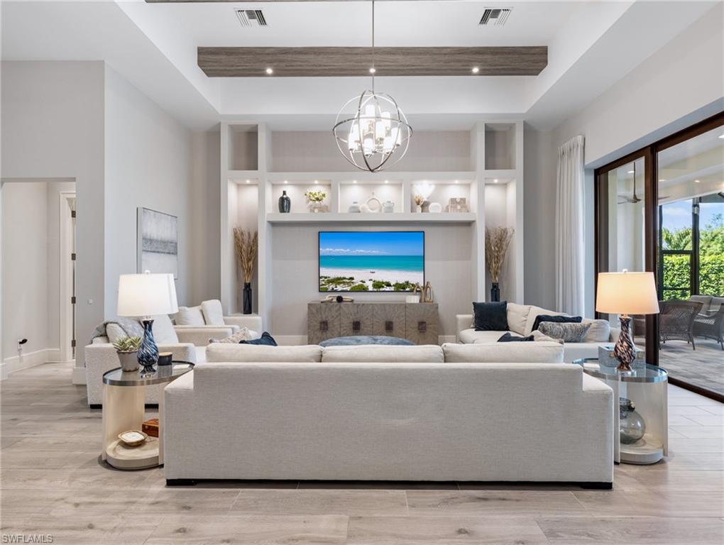 Living room featuring a raised ceiling, light wood-style floors, a high ceiling, a chandelier, and recessed lighting