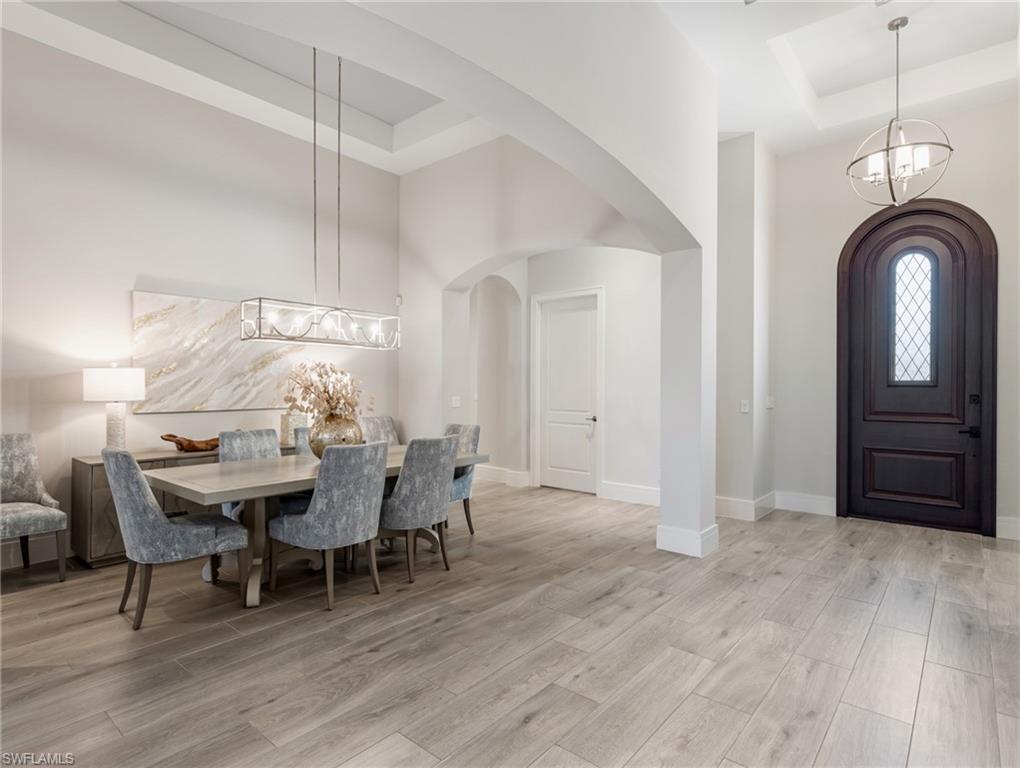 Dining space with a chandelier, a raised ceiling, light wood-type flooring, arched walkways, and a high ceiling