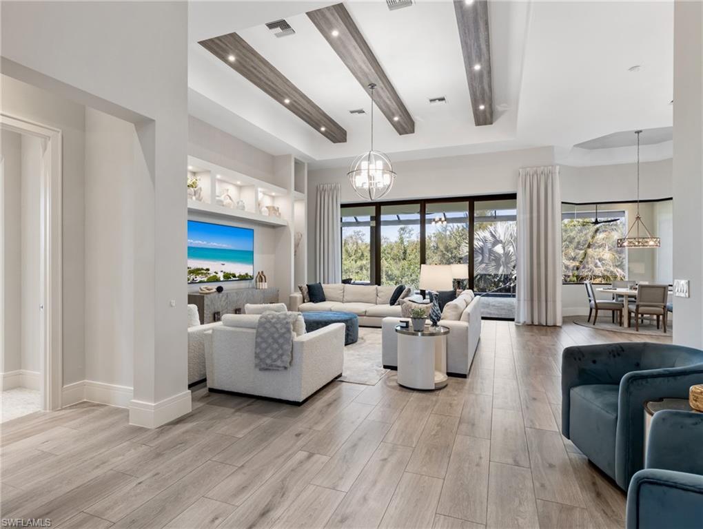 Living room with a chandelier, light wood-style floors, a raised ceiling, and a high ceiling