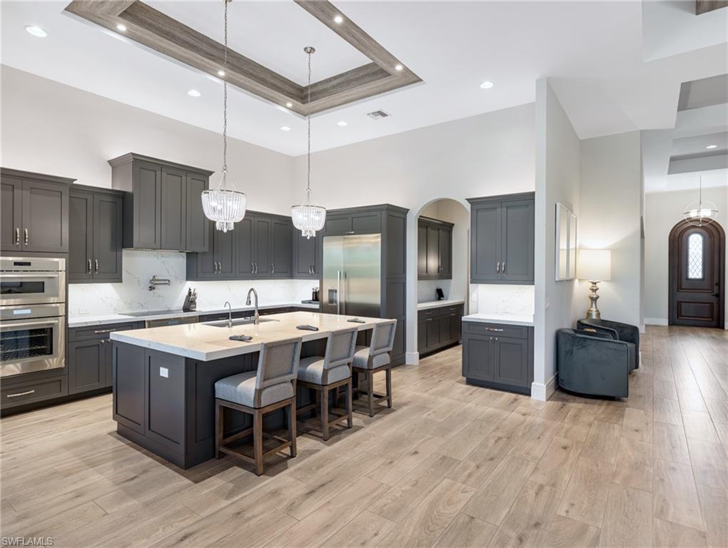 Kitchen featuring a kitchen bar, decorative backsplash, pendant lighting, a tray ceiling, and a high ceiling