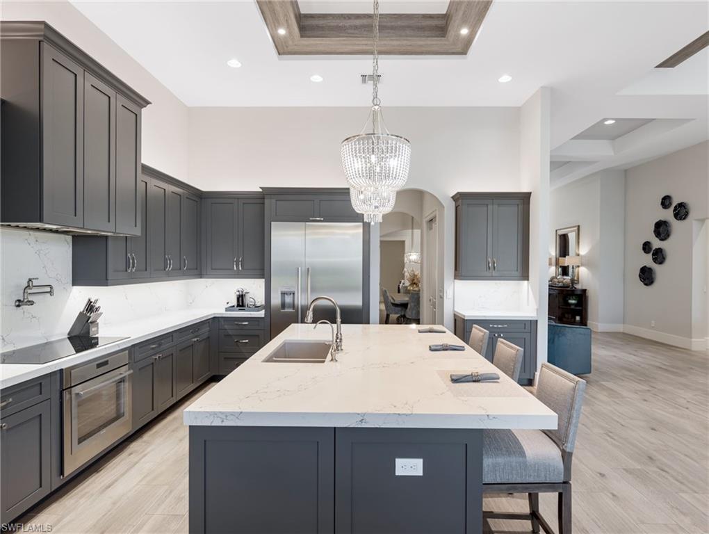 Kitchen featuring light stone counters, a breakfast bar area, gray cabinets, a center island with sink, and a high ceiling