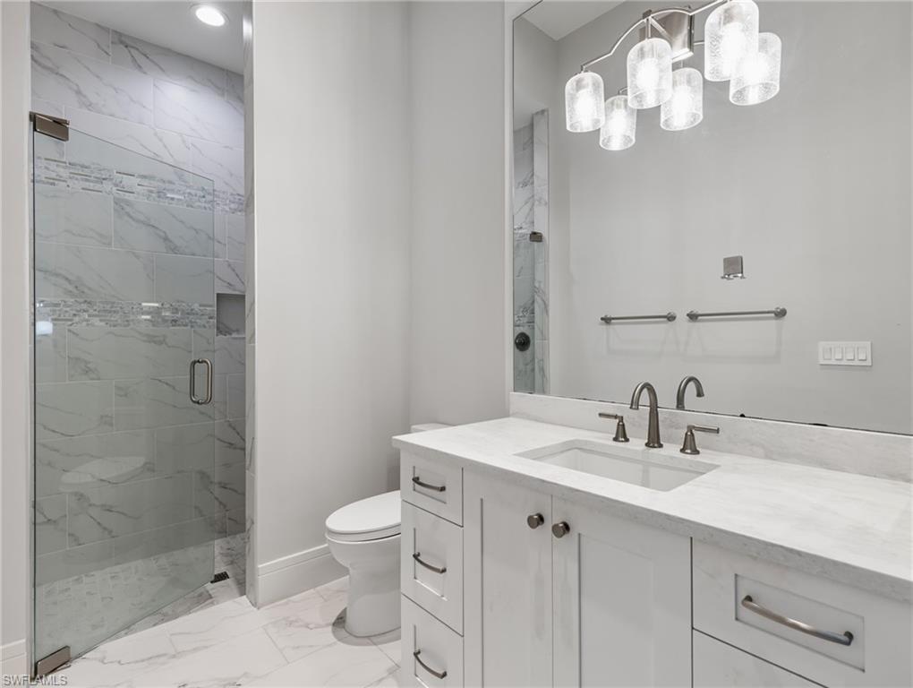 Bathroom featuring vanity, a marble finish shower, and light marble finish flooring