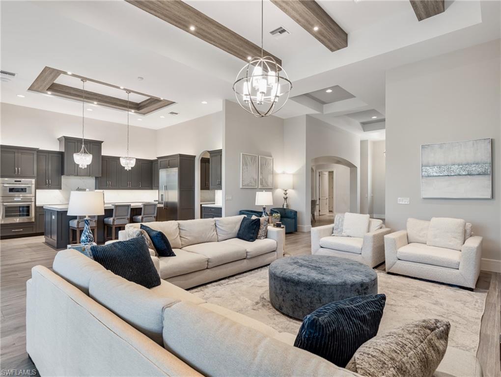 Living area with light wood-style floors, a chandelier, arched walkways, a raised ceiling, and a towering ceiling