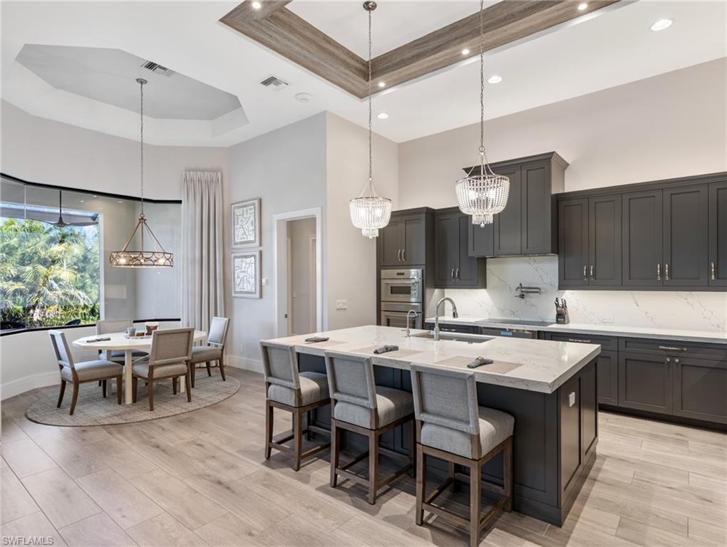 Kitchen featuring a raised ceiling, pendant lighting, a chandelier, light stone countertops, and a towering ceiling