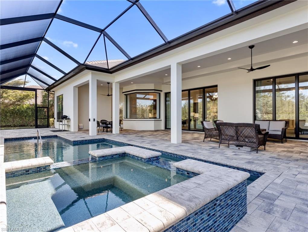 View of pool featuring a sunroom, a pool with connected hot tub, a patio area, an outdoor hangout area, and glass enclosure
