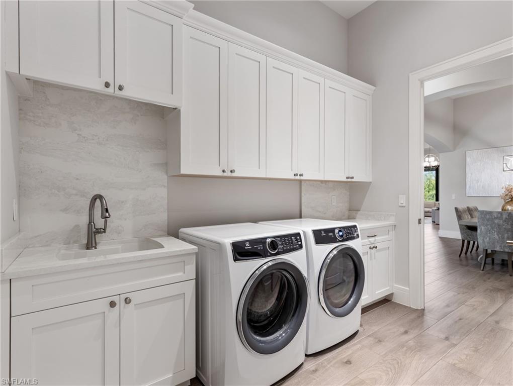 Laundry room featuring light wood-type flooring, washing machine and dryer, a chandelier, arched walkways, and cabinet space