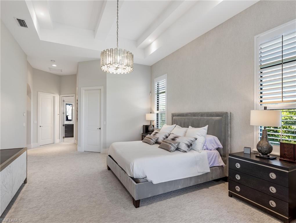 Carpeted bedroom with a chandelier, beamed ceiling, recessed lighting, a towering ceiling, and a tray ceiling