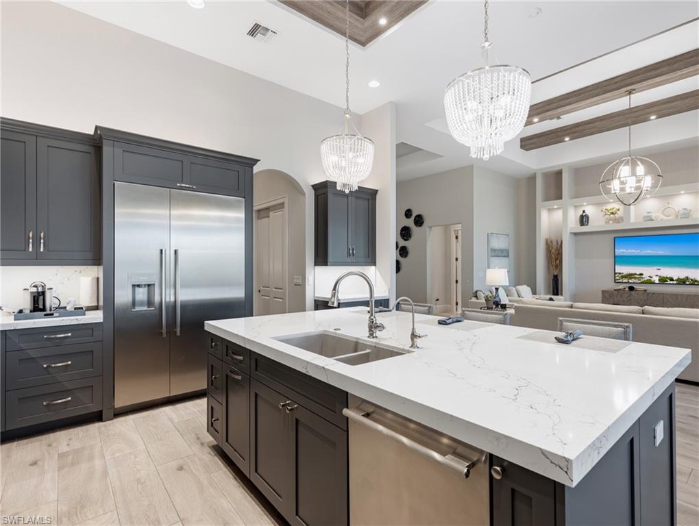 Kitchen with appliances with stainless steel finishes, light stone countertops, light wood-style flooring, a center island with sink, and recessed lighting