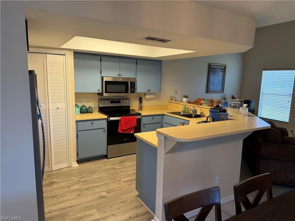 Kitchen featuring a peninsula, stainless steel appliances, light countertops, light wood-style flooring, and a breakfast bar