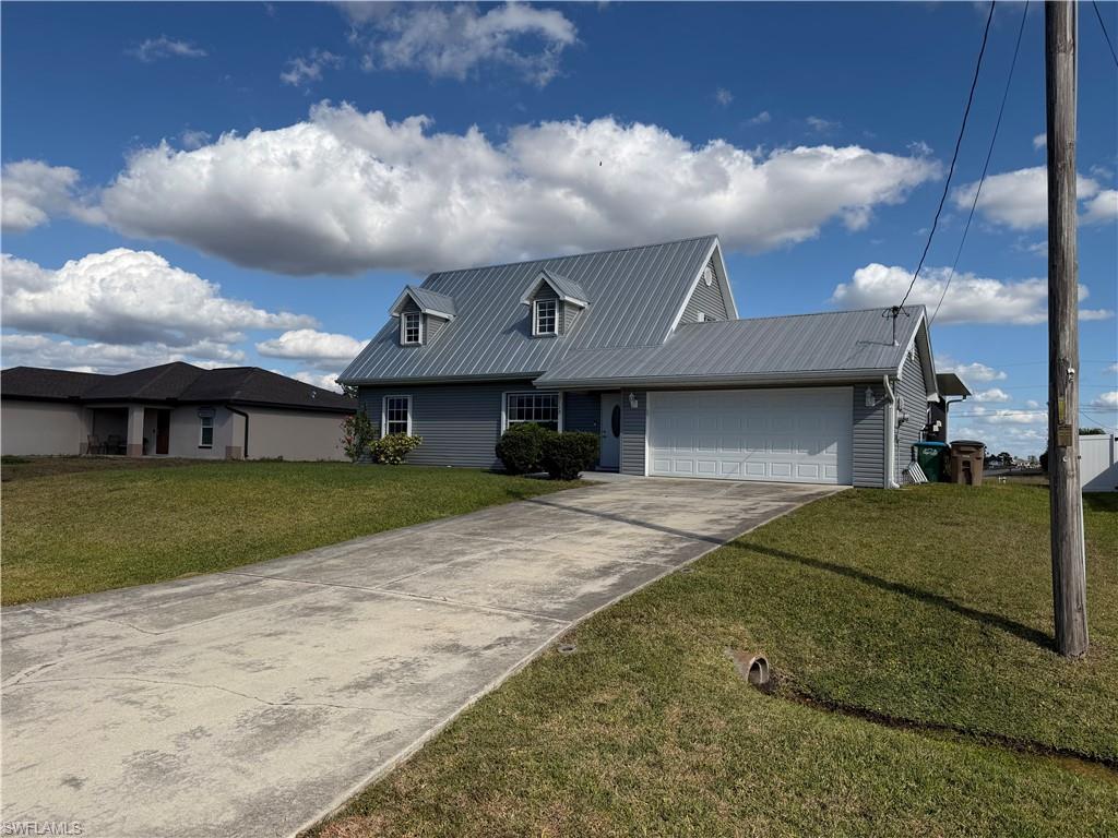 View of front facade featuring a garage, a front lawn, concrete driveway, and a metal roof