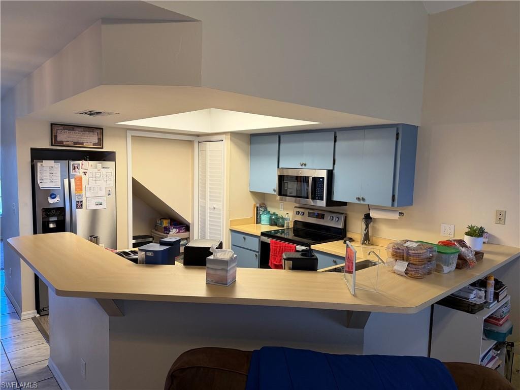 Kitchen featuring blue cabinets, light countertops, a peninsula, appliances with stainless steel finishes, and a breakfast bar