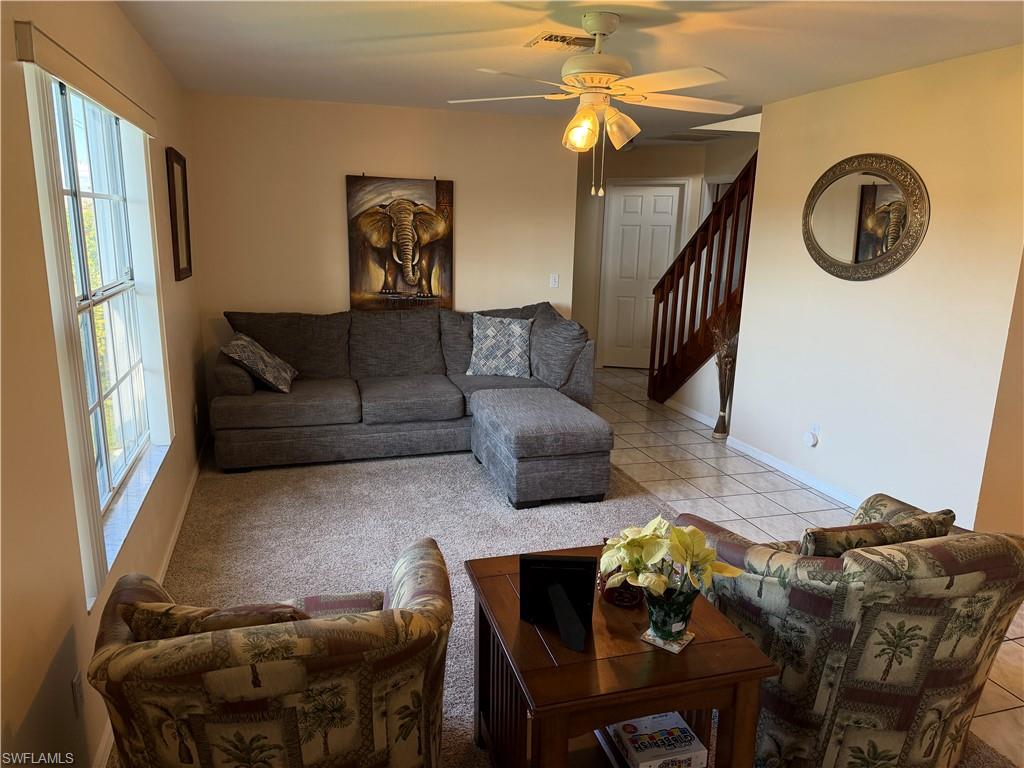 Living area with a ceiling fan, light tile patterned floors, and stairs
