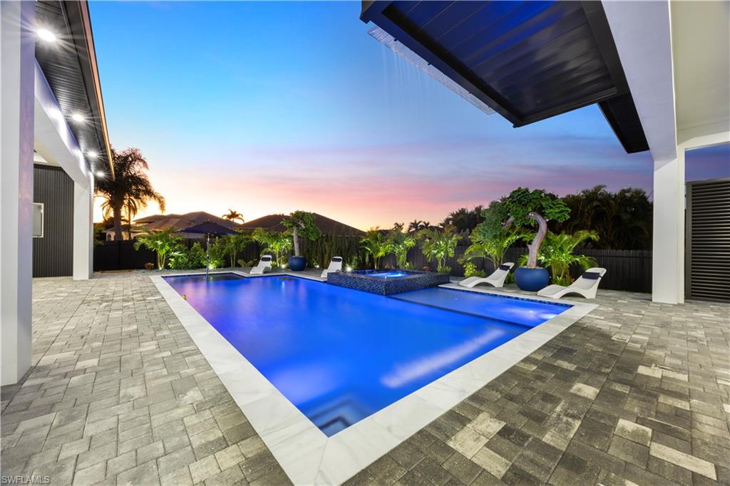 Pool at dusk with a pool with connected hot tub, a fenced backyard, and a patio area