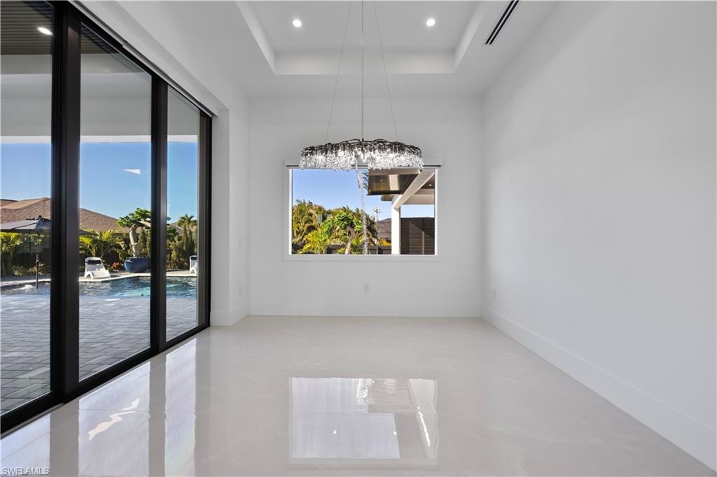 Empty room with a tray ceiling, recessed lighting, and light tile patterned floors