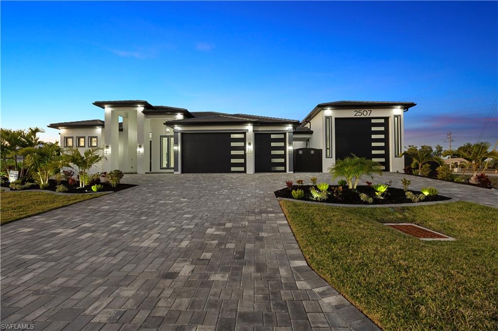 Prairie-style house with a garage, a front lawn, decorative driveway, and stucco siding