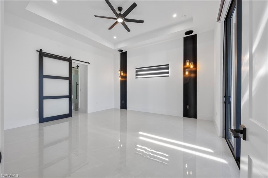 Empty room with a barn door, a raised ceiling, recessed lighting, and a ceiling fan