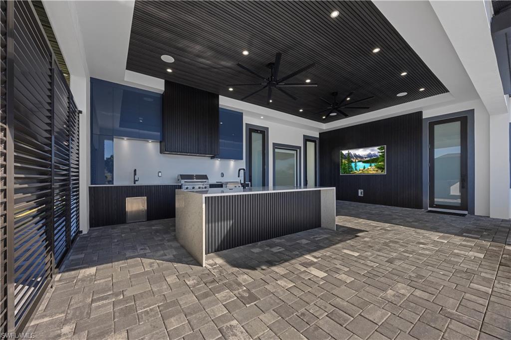 Kitchen featuring modern cabinets, dark cabinets, an island with sink, light stone countertops, and a ceiling fan