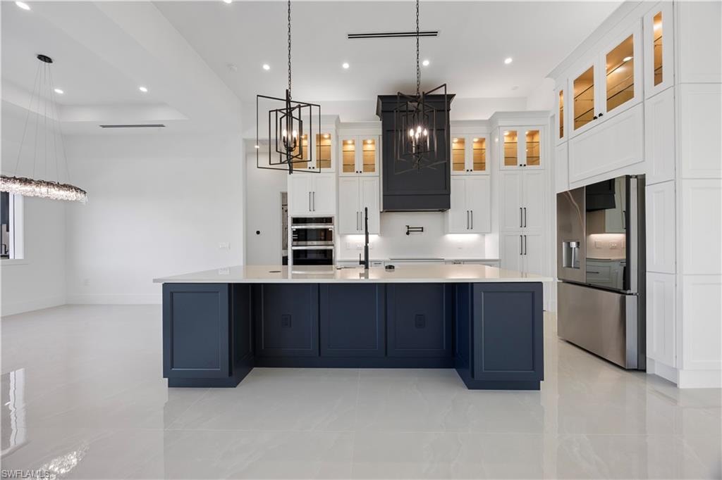 Kitchen with white cabinets, appliances with stainless steel finishes, a chandelier, a large island with sink, and recessed lighting