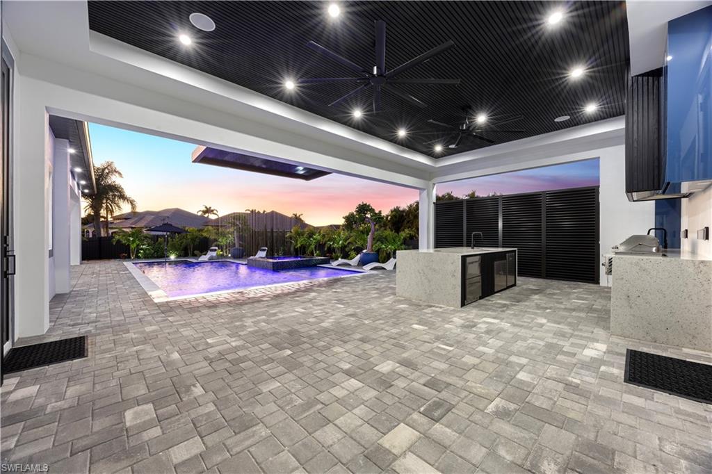 Fenced backyard featuring an outdoor kitchen, a patio area, a pool with connected hot tub, and ceiling fan