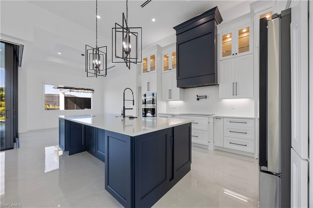Kitchen with white cabinets, glass insert cabinets, hanging light fixtures, a kitchen island with sink, and appliances with stainless steel finishes
