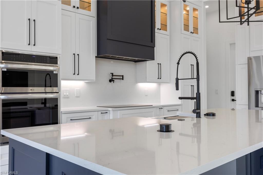 Kitchen with stainless steel appliances, white cabinets, glass insert cabinets, and light stone counters