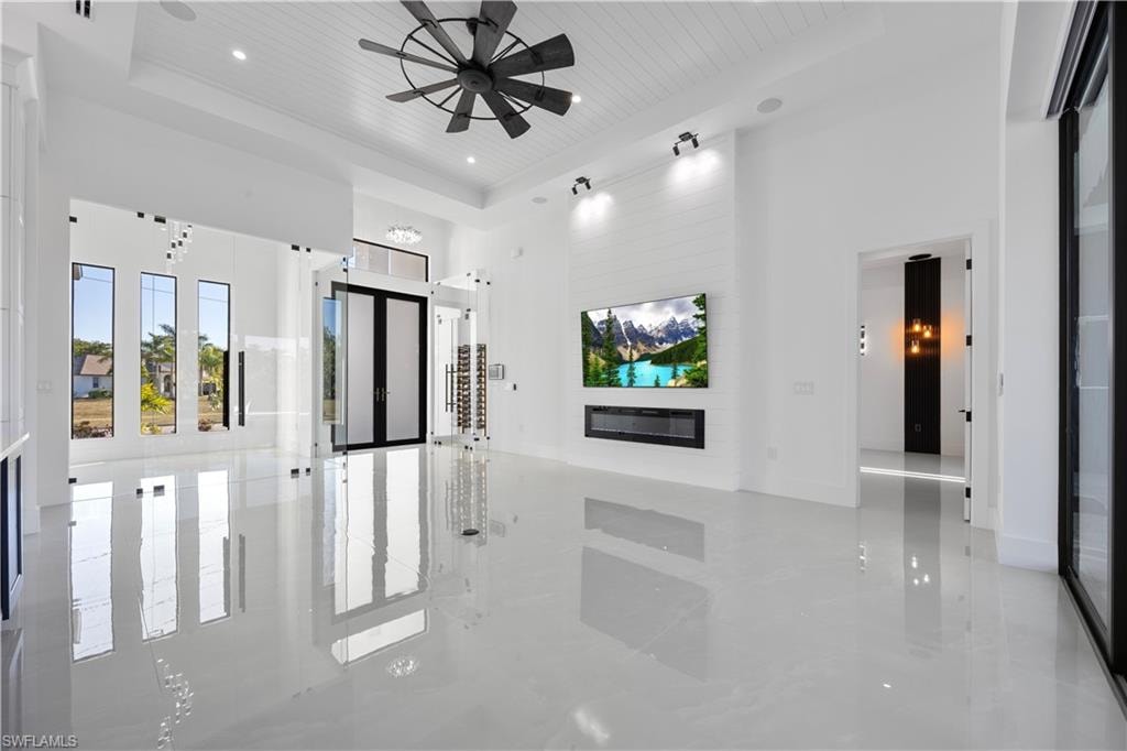 Unfurnished living room with a high ceiling, wood ceiling, a tray ceiling, a fireplace, and ceiling fan