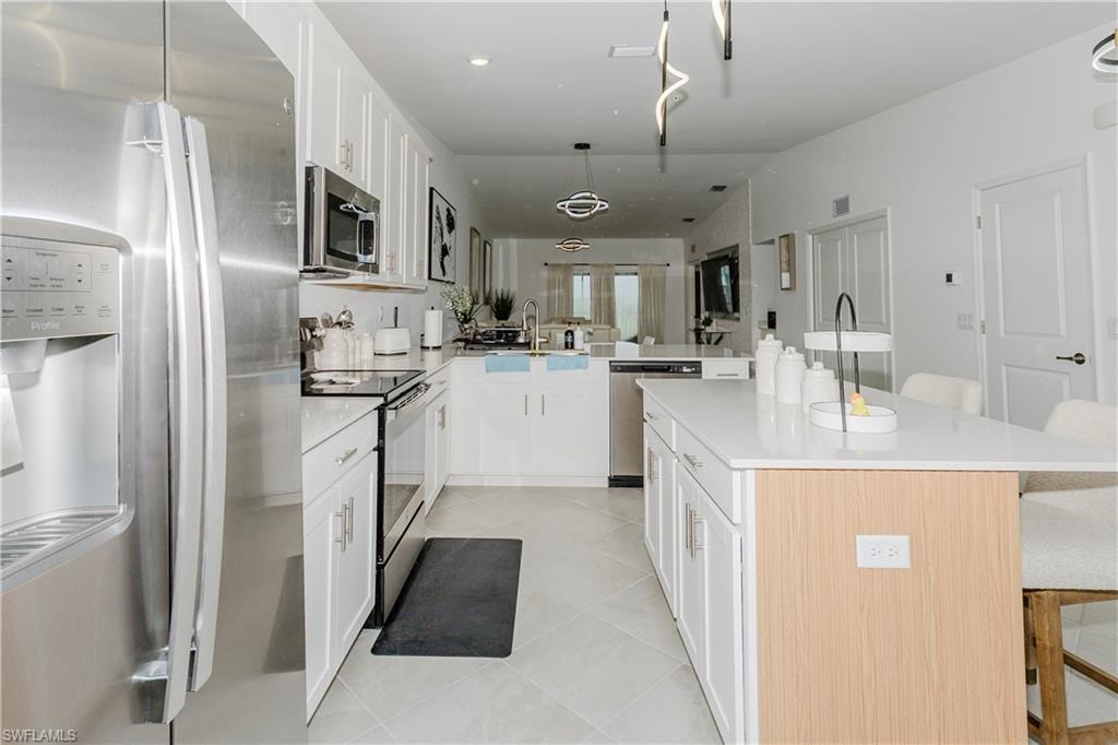 Kitchen with appliances with stainless steel finishes, a breakfast bar, a peninsula, light tile patterned floors, and light countertops