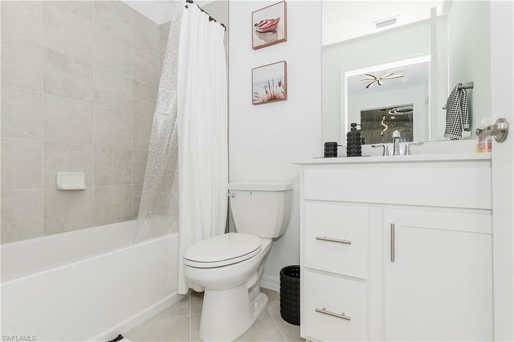 Bathroom with tile patterned floors, toilet, vanity, shower / tub combo with curtain, and baseboards